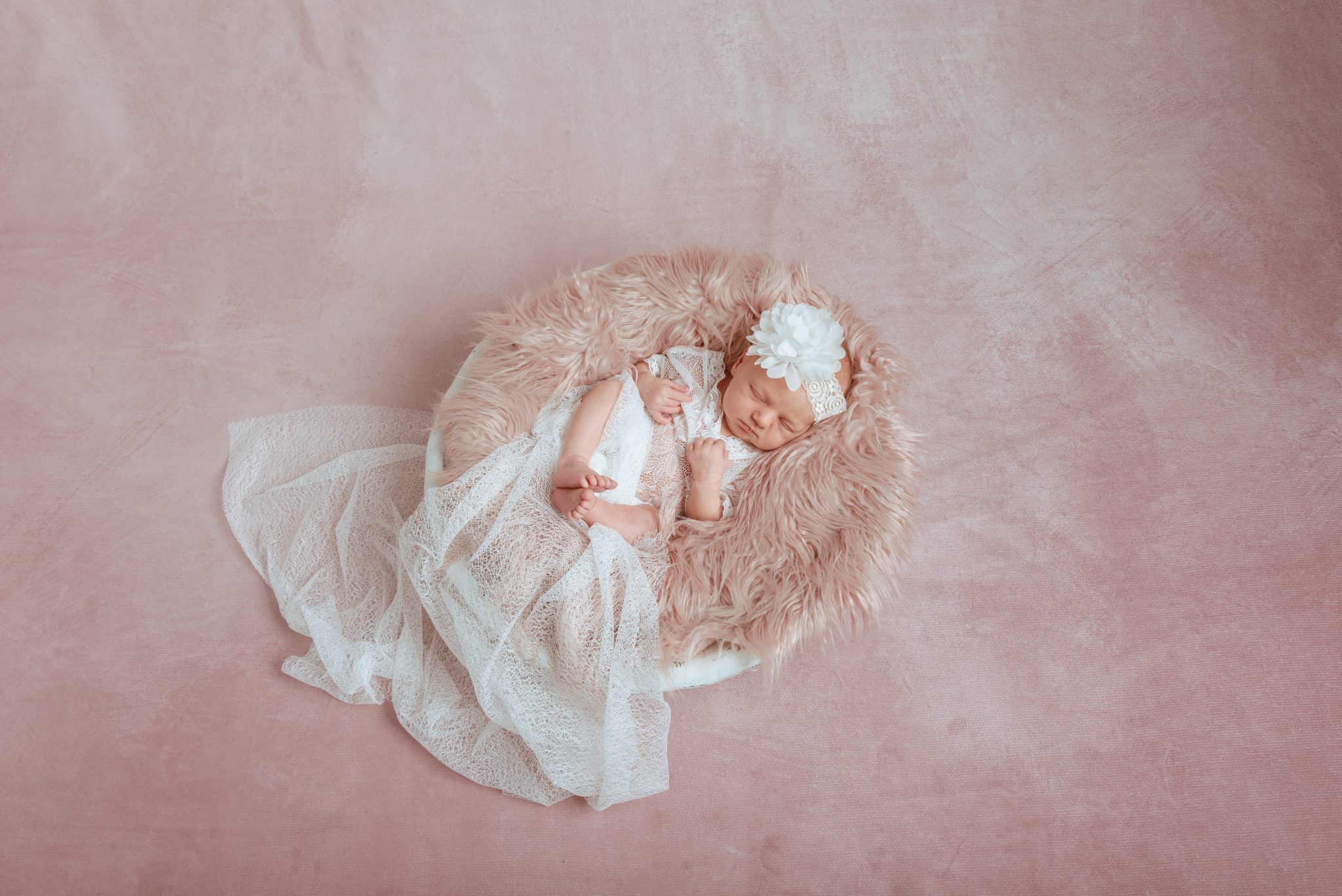 Tyttövauva nukkuu pehmeässä korissa pinkillä taustalla